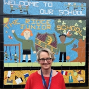 Image shows Beverly Furbur from The Ridge Primary school smiling infront of a sign wearing a red top