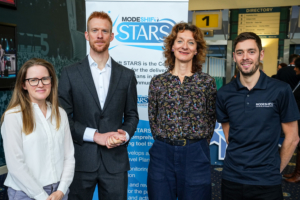 Team of 3 from SYMCA including Ed Clancy wearing a suit smiling stood in front of a Modeshift STARS pull up banner with Tom Murray from Modeshift wearing a blue T-shirt