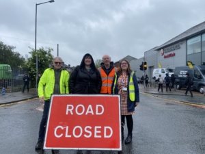 Four people wearing vis vests and raincoats stood behind a red Road Closed sign on a road