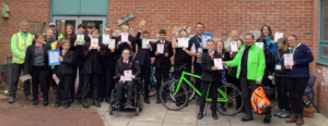 Group of students stood together with staff and a green bike smiling holding up a certificate 